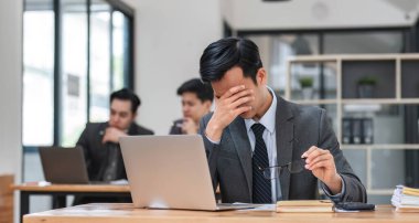 Ofis lobisinde dizüstü bilgisayar kullanarak ciddi bir profesyonele odaklanmış. Arka planda dizüstü bilgisayar kullanan Asyalı genç bir adam. Kablosuz teknoloji kavramı..