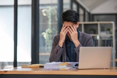 Üzücü depresyon, işten ciddi insanlar, stres kavramı. Asyalı adam bilgisayarlı çalışma yerini kullanarak sıkıntı çekiyor. Küresel ekonomi, sağlık sorunları...