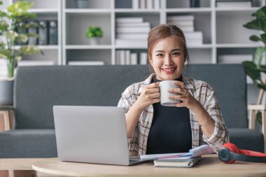 Güzel ve ilham verici Asyalı kadın hafta sonları oturma odasında dizüstü bilgisayarında çalışıyor....