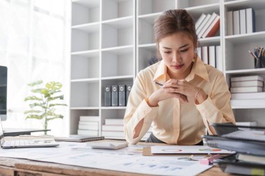 Stresli genç Asyalı iş kadını masasındaki mali yatırım raporlarını yeniden kontrol etmeye odaklanıyor...