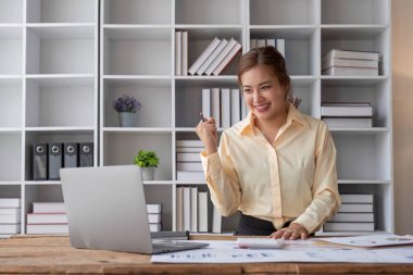 Heyecanlı Asyalı kadın dizüstü bilgisayarla masada oturuyor ve başarıyı kutluyor...