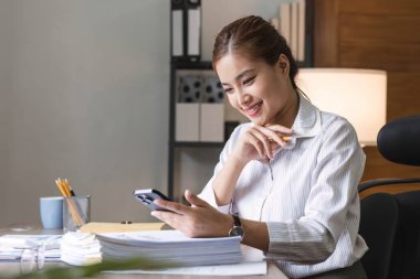 Genç Asyalı kadın evde dizüstü bilgisayarla çalışırken cep telefonu kullanıyor. Bilgisayardaki arkadaşlarla görüntülü konuşma sırasında kadın arama sitesi, akıllı telefon ile mesajlaşma veya alışveriş..