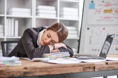 İşten yorgun düşmüş Asyalı iş kadını ofiste masanın üstünde uyuyor.