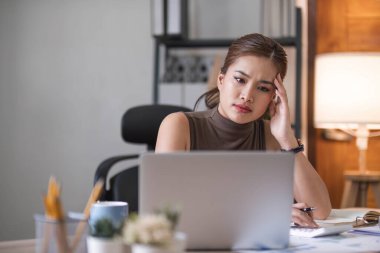 Dizüstü bilgisayarda çalışan Asyalı genç iş kadını. Başı ağrıyor ve ofiste çalışırken çok düşünüyor....