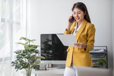 Genç meşgul Asyalı iş kadını modern ofiste telefonla konuşuyor. Asyalı iş kadını şirket satış müdürü takım elbise giyiyor iş yerinde cep telefonuyla konuşuyor....