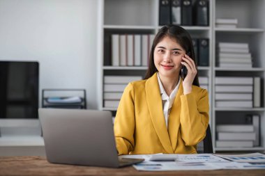 Genç meşgul Asyalı iş kadını modern ofiste telefonla konuşuyor. Asyalı iş kadını şirket satış müdürü takım elbise giyiyor iş yerinde cep telefonuyla konuşuyor....