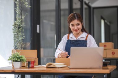 İnternet üzerinden nakliye alışverişi, iş yerindeki karton kutuya adres yazan küçük işletme sahibi gençler. Küçük işletme girişimcisi KME ya da ofiste kutuyla çalışan serbest çalışan Asyalı kadın..