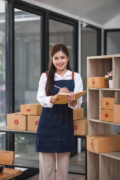 başlangıçta küçük işletme KOBİ, Girişimci mutlu sahibi dizüstü bilgisayara bakar ve teslimat için kutuya müşteri adresi yazar