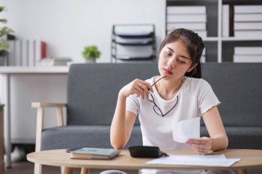 Asyalı kadın, evdeki kanepede oturan hesap makinesiyle elinde tuttuğu fatura hesaplama masraflarını vurguladı...