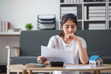 Asyalı kadın, evdeki kanepede oturan hesap makinesiyle elinde tuttuğu fatura hesaplama masraflarını vurguladı...