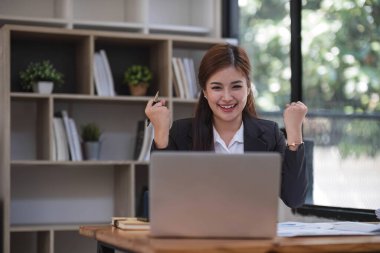 Güzel Asyalı iş kadını ofisteki dizüstü bilgisayarını kullanarak bunu kutluyor ve keyif veriyor. Küçük bir iş kurma ve başarılı bir konsept...