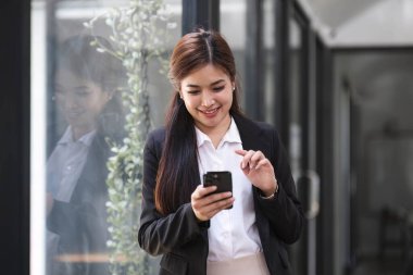 Ofiste elinde kağıtlar ve cep telefonuyla gülümseyen çekici Asyalı kadın....