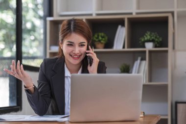 Ofisteki resmi takım elbiseli Asyalı iş kadını akıllı telefon ve çalışma süresince mutlu ve neşeli...