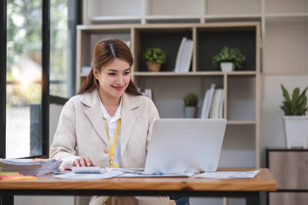 stock image Asian Businesswoman Using laptop computer and working at office with calculator document on desk, doing planning analyzing the financial report, business plan investment, finance analysis concept...