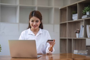 Güzel bir Asyalı kadın elinde akıllı telefon tutuyor ve online alışveriş için kredi kartı kullanıyor.