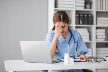 Dizüstü bilgisayara bakıp internette kötü haber okuyan stresli genç bayan doktor iş yerinde hata yapmaktan korkuyor. Gerginlik içindeki mutsuz profesyonel doktor iş yerinde bilgisayar problemi çözmekten yoruldu...