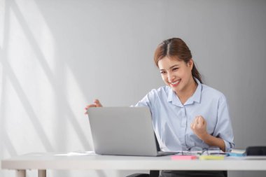 Asyalı iş kadınları, modern bir ofiste dizüstü bilgisayarla mutlu bir şekilde gülümseyen iş yerinde neşeli bir başarı ifadesi sergilerler....