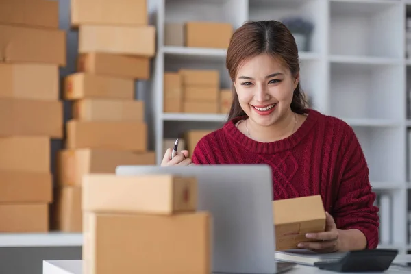 stock image Starting small business entrepreneur of independent Asian woman smiling using computer laptop with cheerful success of online marketing package box items