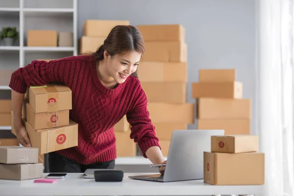 Starting small business entrepreneur of independent Asian woman smiling using computer laptop with cheerful success of online marketing package box items