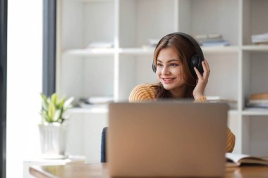 Kulaklıklı Asyalı bir kadın internetten ders çalışmaya ara verip iş sırasında müzik dinlemekten mutlu bir şekilde müzik dinliyor.