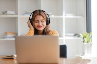 Kulaklıklı Asyalı bir kadın internetten ders çalışmaya ara verip iş sırasında müzik dinlemekten mutlu bir şekilde müzik dinliyor.
