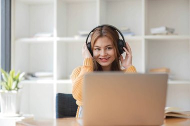 Kulaklıklı Asyalı bir kadın internetten ders çalışmaya ara verip iş sırasında müzik dinlemekten mutlu bir şekilde müzik dinliyor.
