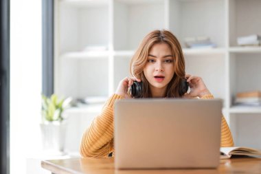Kulaklıklı Asyalı bir kadın internetten ders çalışmaya ara verip iş sırasında müzik dinlemekten mutlu bir şekilde müzik dinliyor.