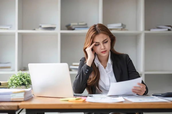 stock image A stressed and serious young Asian businesswoman focuses on working on her business financial reports at her desk in the office...