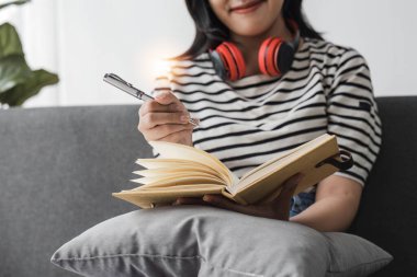 Kulaklıklı genç Asyalı kadın evde dinleniyor. Müzik dinliyordum. rahat bir kanepeye oturmuş kulaklık takıyorum...