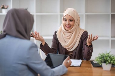 Profesyonel ve kendinden emin bir Asyalı Müslüman iş kadını iş arkadaşıyla ofiste iş tartışıyor....