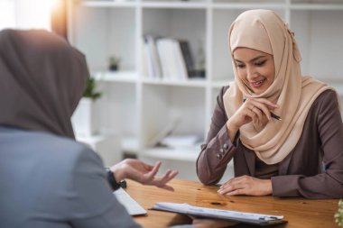 Profesyonel ve kendinden emin bir Asyalı Müslüman iş kadını iş arkadaşıyla ofiste iş tartışıyor....