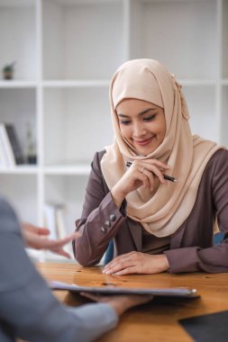 Profesyonel ve kendinden emin bir Asyalı Müslüman iş kadını iş arkadaşıyla ofiste iş tartışıyor....
