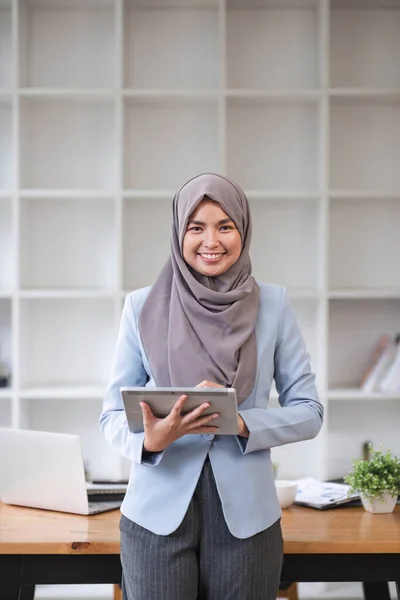 stock image A portrait of a successful Asian Muslim businesswoman stands in her modern office with a digital tablet in her hand...