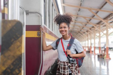Gezgin Afro-Asyalı Amerikalı kadın trene atlamak için trene biniyor. Trenin kapısında dikilen genç kadın kapıdan dışarı bakıyor, tren istasyonunda turist.