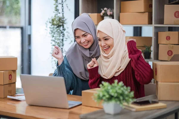 Stock image Two women muslim look at online product sales data on laptops and show joy..