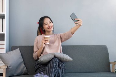 Kanepede oturan ve evinde selfie çeken genç bir kadın..