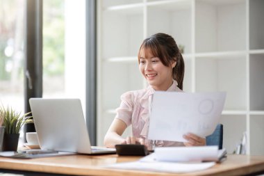 Asyalı iş kadını dizüstü bilgisayar kullanıyor ve çalışıyor. Muhasebe analizi yapan iş kadını yatırım verilerini rapor ediyor..