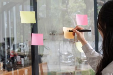 Kapalı kapılar ardında ofis duvarına yapışkan notlar yazan iş kadını..