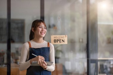 Başarılı küçük işletme sahibi. Kahve dükkanında elinde tabletle duran önlüklü güzel bir kız. Asyalı kadın kahveci kafe sahibinin portresi..