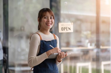 Başarılı küçük işletme sahibi. Kahve dükkanında elinde tabletle duran önlüklü güzel bir kız. Asyalı kadın kahveci kafe sahibinin portresi..