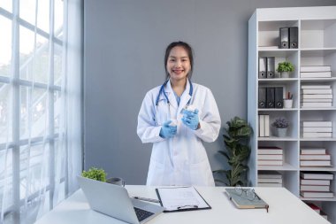 Genç, güzel doktor elinde ilaç şişesiyle klinikte laptopla tıbbın detaylarını anlatıyor..