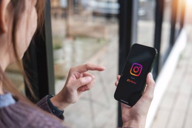 CHIANG MAI, THAILAND - JUL 7, 2023: A woman holds Apple iPhone X with Instagram application on the screen at cafe. Instagram is a photo sharing app for smartphones.. clipart