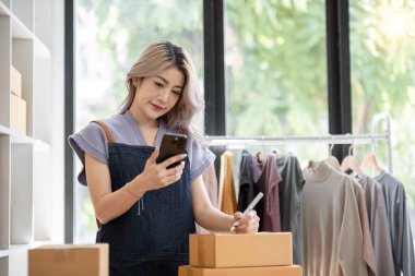 Kadın girişimci telefonda konuştuktan sonra paketin üzerine yazı yazıyor ve online satıcı konseptindeki paket üzerine yazı yazıyor..