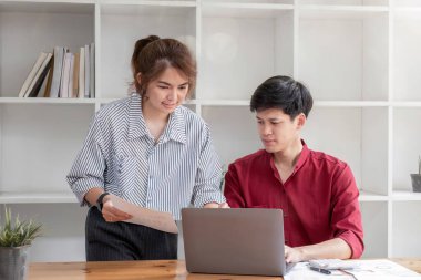 İş adamı ve meslektaşı ofiste yan yana otururken dizüstü bilgisayarda çalışmayı tartışıyor...