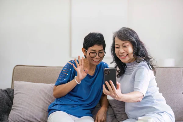 Two 60-year-old Asian women chatting with friends via video call..