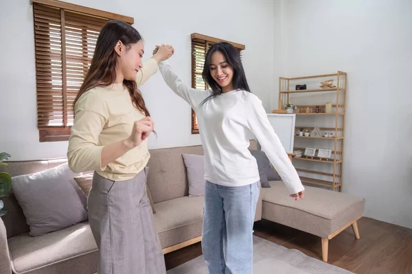 Beautiful young Asian lesbian couple dancing in the living room at home, fun mood. LGBT concept of sex and happy living together.