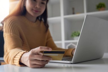 Genç Asyalı kadın bilgisayardan alışveriş yapmak için kredi kartı kullanıyor..