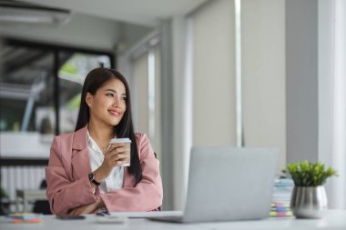 İş kadını, sabahları ofiste bir fincan kahve içerken dizüstü bilgisayarla çalışıyor...