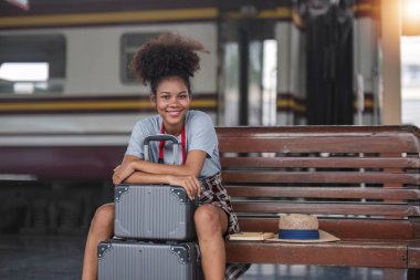 Asyalı Afrikalı bayan turist elinde cep telefonuyla tren istasyonunda oturuyor. İstasyonda akıllı telefon dizüstü bilgisayarı oynayan kendine güvenen genç kız.