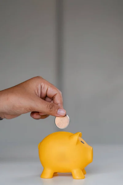 Close up woman puts coins in a piggy bank with a pile of coins to save money..